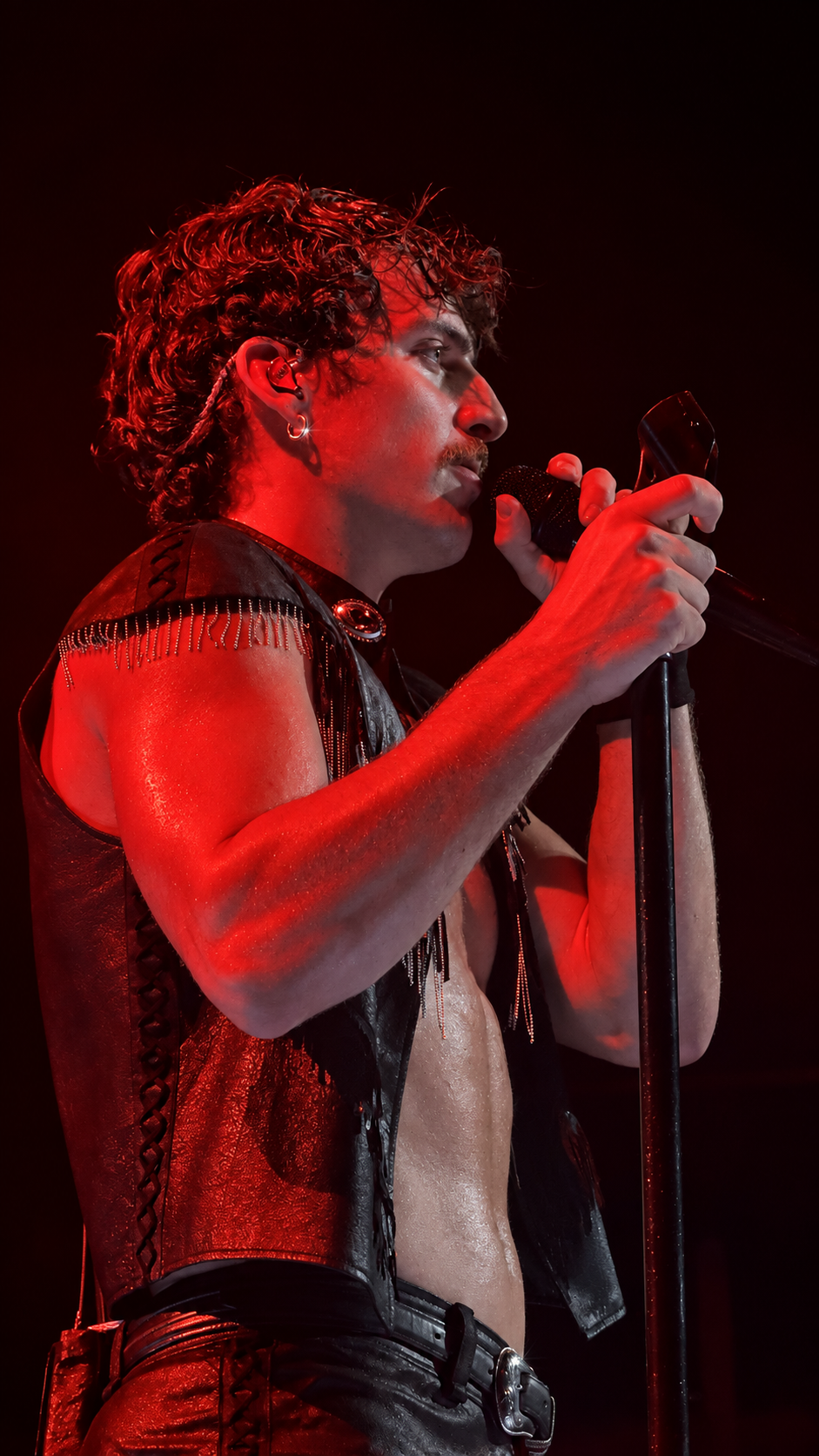 Close-up of a singer holding a microphone under deep red stage lighting